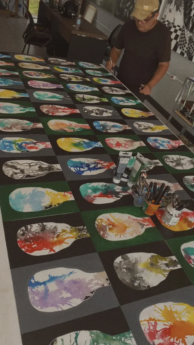 Mesa do ateliê com dezenas de pequenas pinturas coloridas
