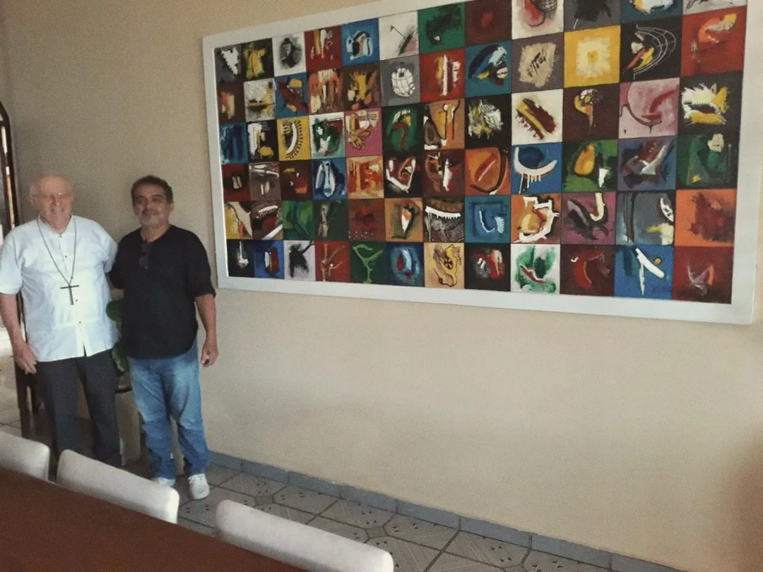 Dom Carlos Verzeletti e Almir diante de uma grande obra com dezenas de quadros coloridos
